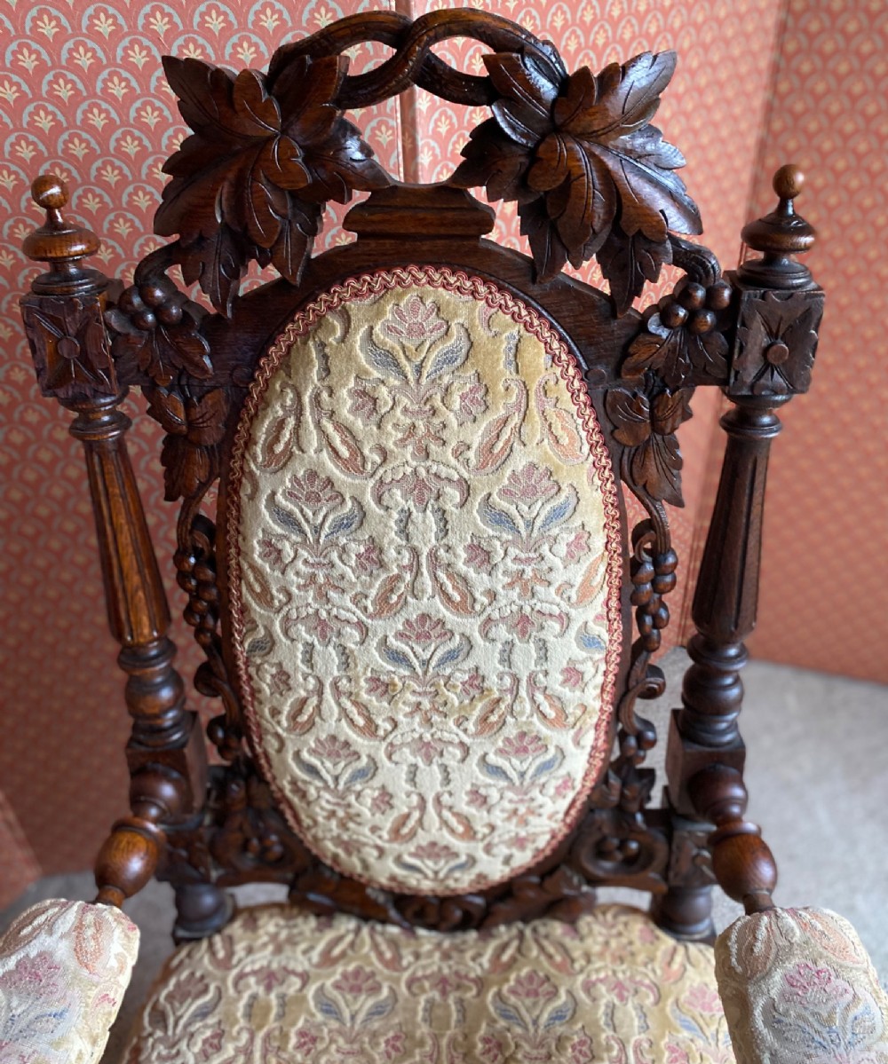 A 19th-century carved dark oak armchair with an oval upholstered backrest, ornate leaf cresting, and scrolled armrests. View II