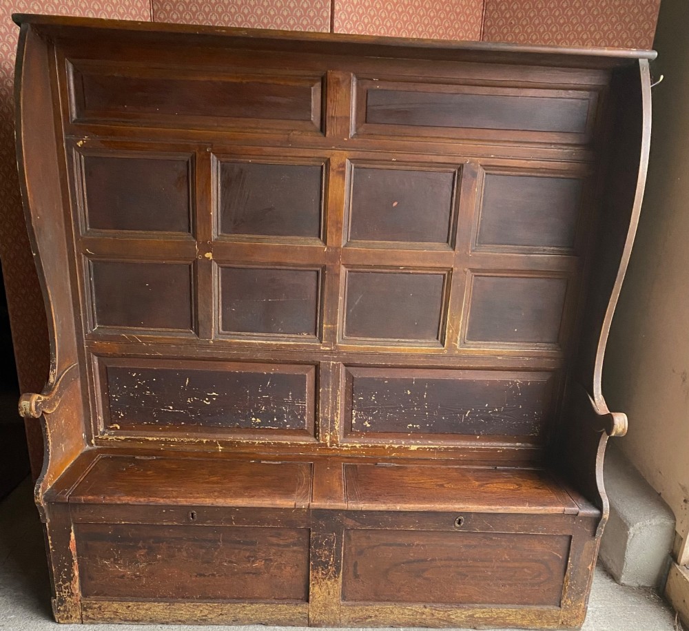An 18th-century high-backed wooden settle featuring multi-panelled backboards, wing sides, and a lift-up box seat base with rich brown patina.