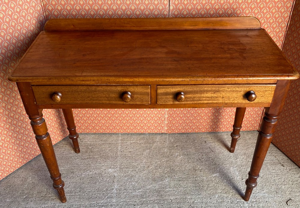 A Victorian warm brown mahogany writing desk featuring two frieze drawers with turned wooden knobs, supported by turned tapered legs and a low gallery backboard.