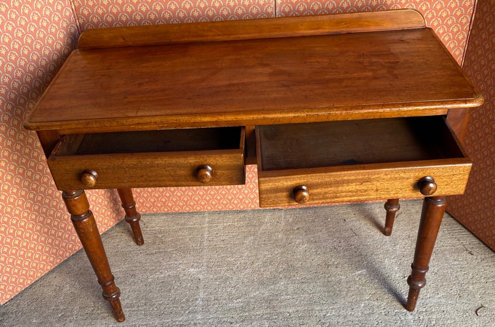 A Victorian warm brown mahogany writing desk featuring two frieze drawers with turned wooden knobs, supported by turned tapered legs and a low gallery backboard. View II