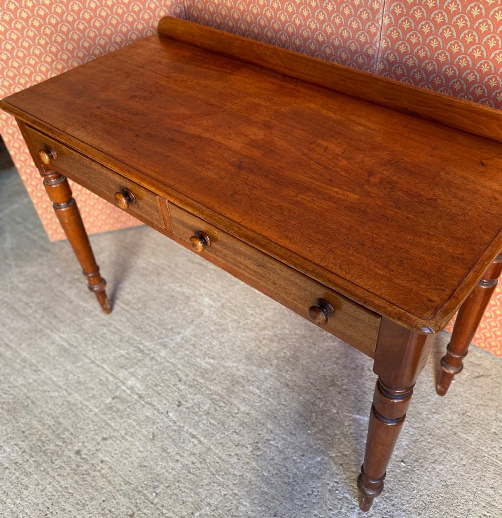A Victorian warm brown mahogany writing desk featuring two frieze drawers with turned wooden knobs, supported by turned tapered legs and a low gallery backboard. View IV