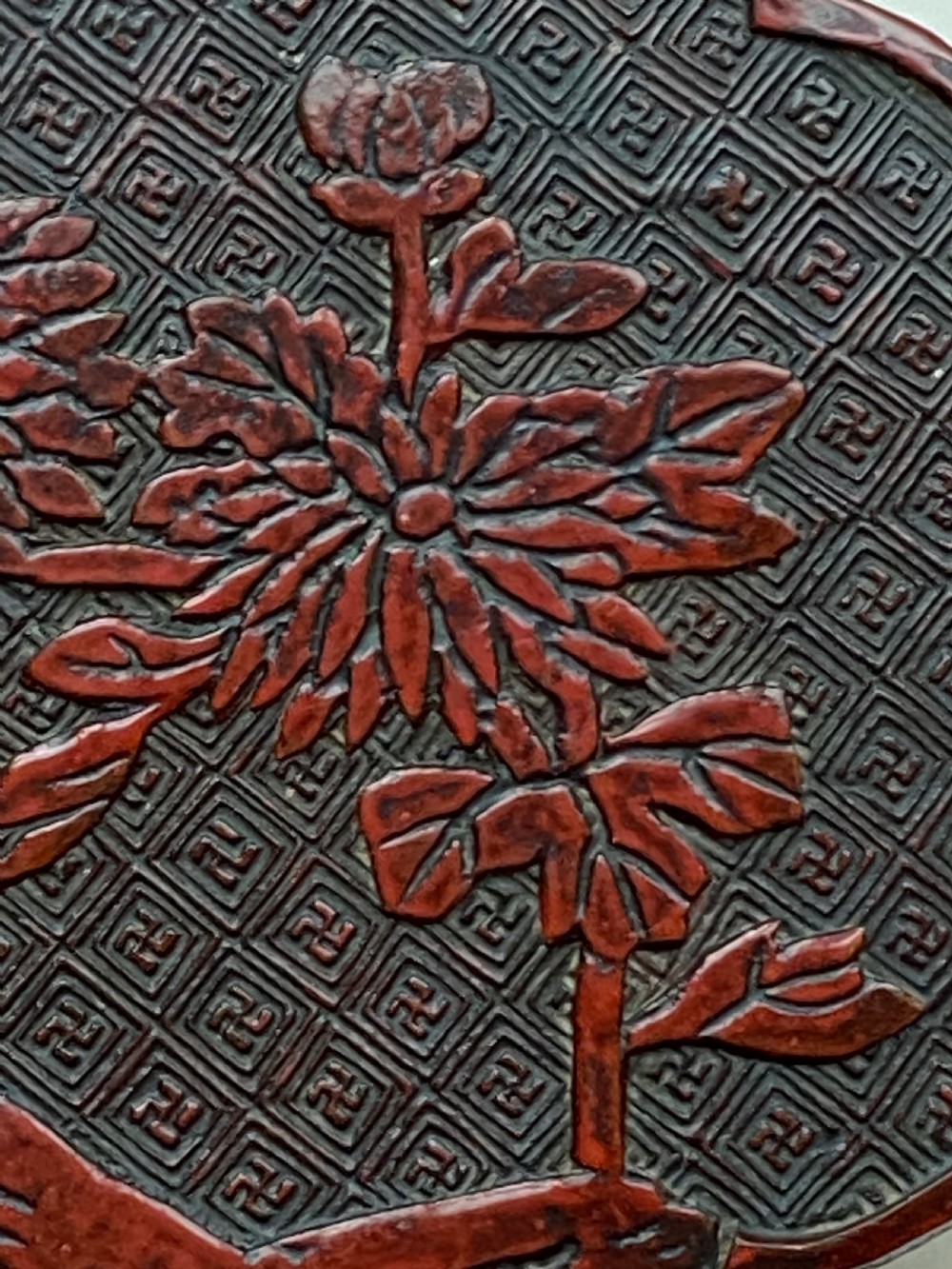 A lobed Qing Dynasty carved red cinnabar lacquer lidded box decorated with chrysanthemum blossoms and rockwork over a dark diaper background. View III