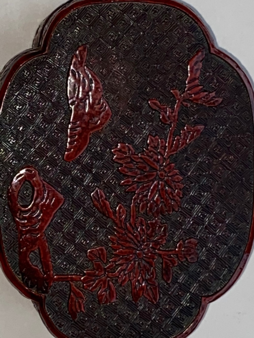 A lobed Qing Dynasty carved red cinnabar lacquer lidded box decorated with chrysanthemum blossoms and rockwork over a dark diaper background. View IV
