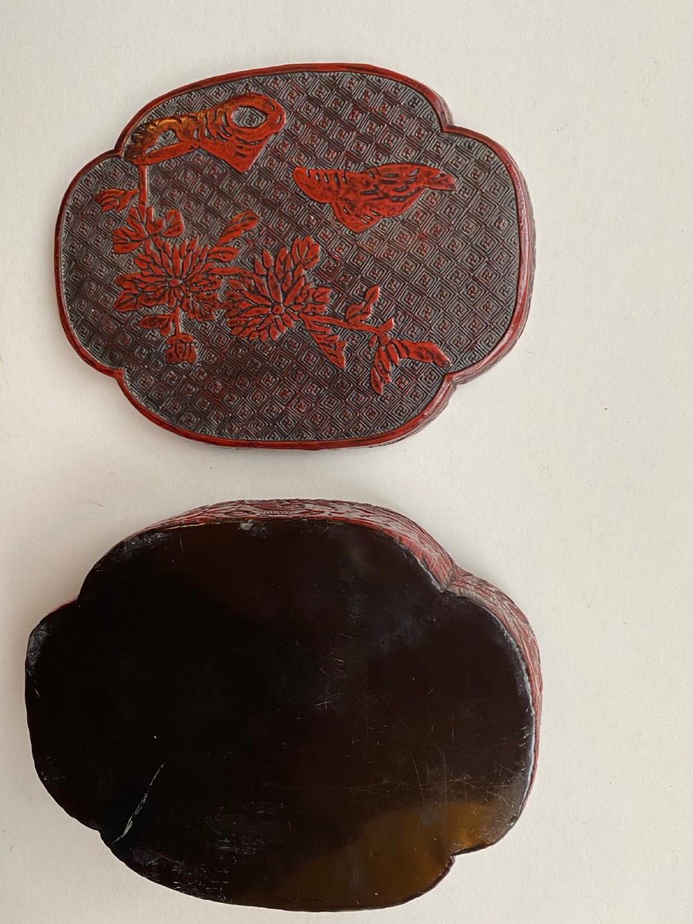 A lobed Qing Dynasty carved red cinnabar lacquer lidded box decorated with chrysanthemum blossoms and rockwork over a dark diaper background. View IX