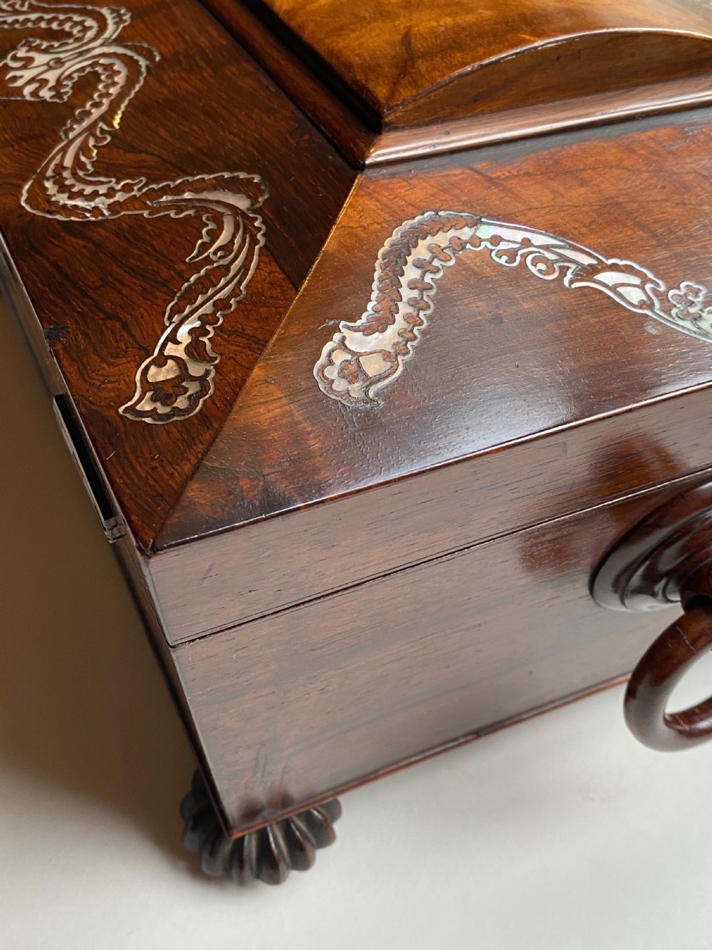 A Regency rosewood workbox with mother-of-pearl foliate inlays, side ring handles, and carved feet. View X