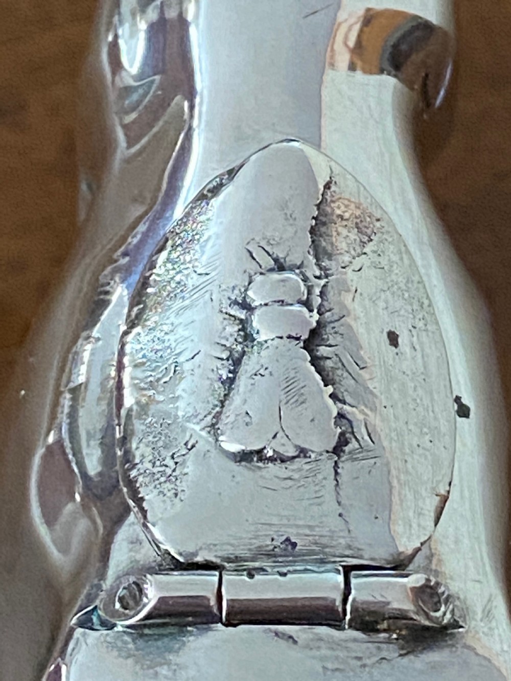A sculpted silver cow creamer featuring a hollow body, looped tail handle, curved horns, and a hinged flap on its back. View V