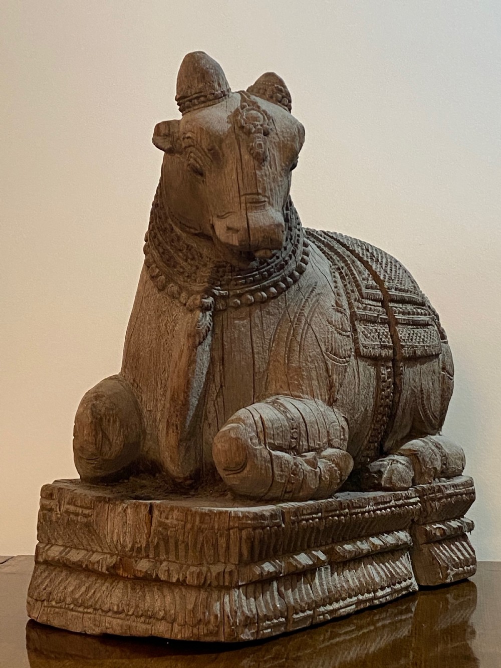 A carved wooden sculpture of a seated Nandi bull on a decorated plinth featuring intricate neck garlands and a saddle cover. View II