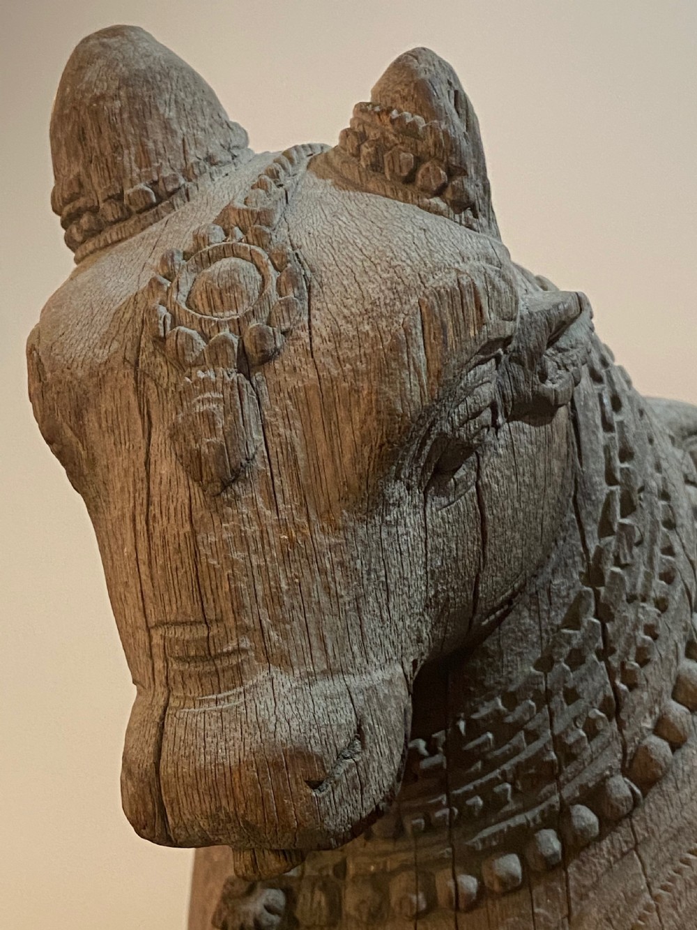 A carved wooden sculpture of a seated Nandi bull on a decorated plinth featuring intricate neck garlands and a saddle cover. View IV