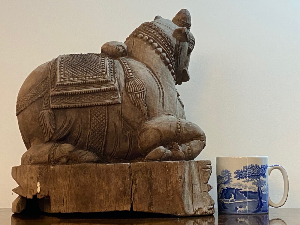 A carved wooden sculpture of a seated Nandi bull on a decorated plinth featuring intricate neck garlands and a saddle cover. View IX