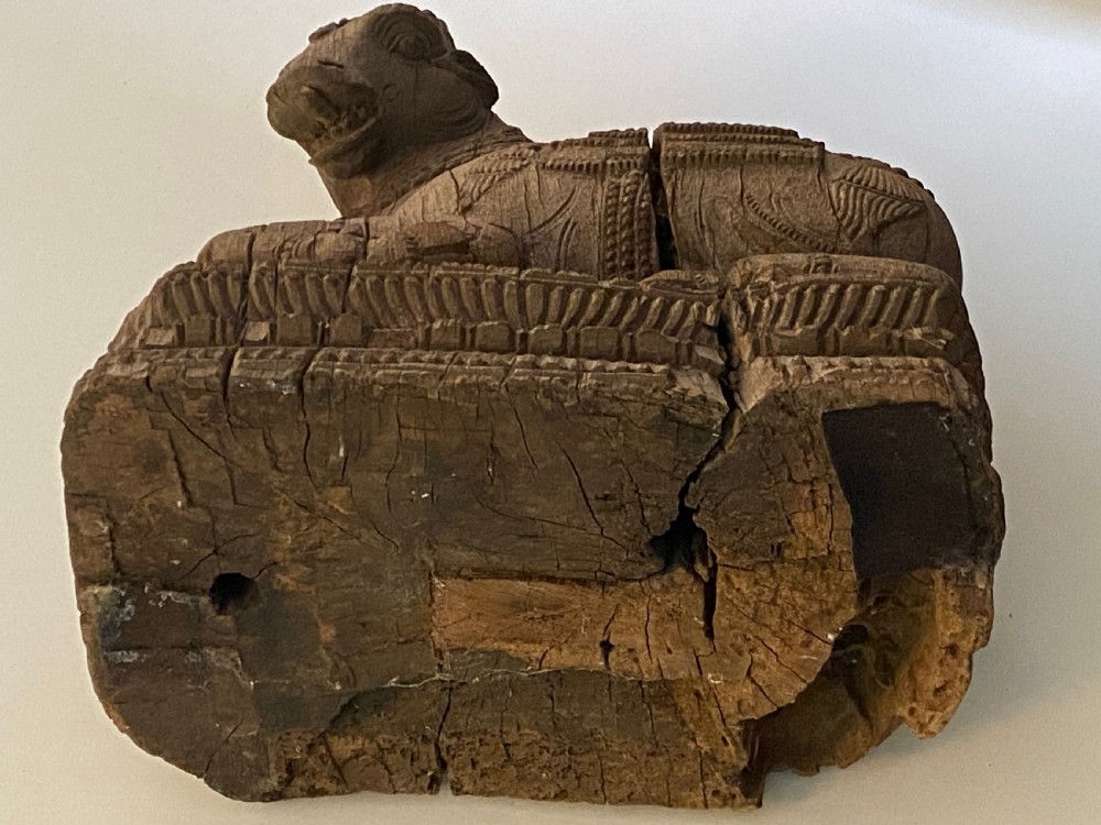 A carved wooden sculpture of a seated Nandi bull on a decorated plinth featuring intricate neck garlands and a saddle cover. View XI