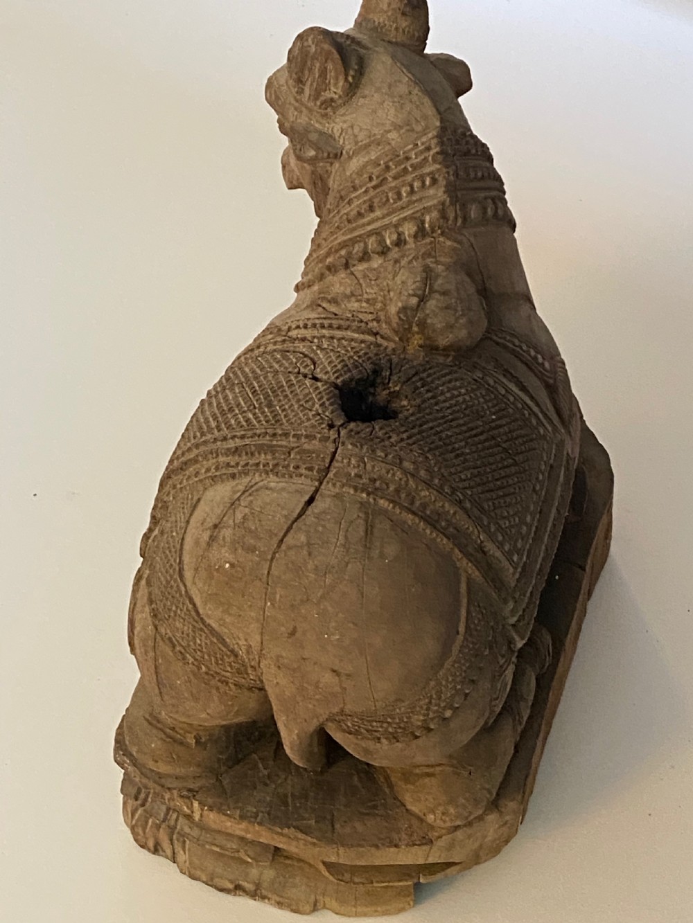 A carved wooden sculpture of a seated Nandi bull on a decorated plinth featuring intricate neck garlands and a saddle cover. View XII