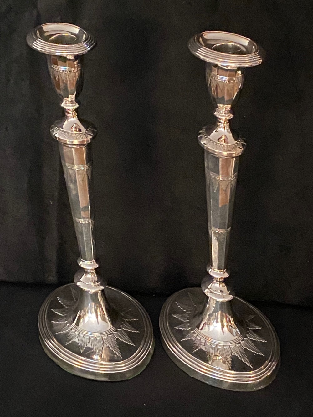 A pair of George III silver-plated candlesticks featuring faceted tapering shafts and circular stepped bases holding white candles. View XII