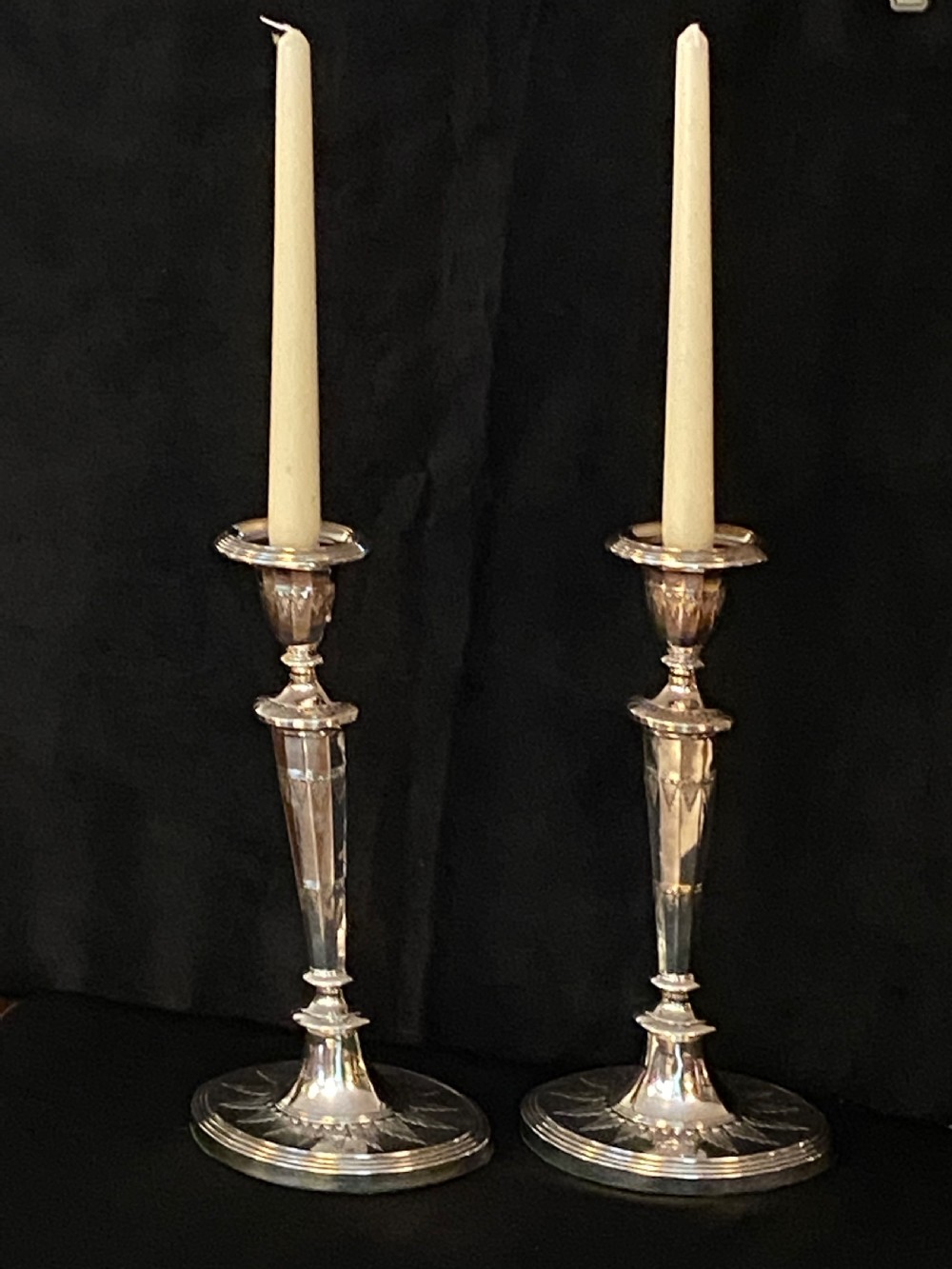 A pair of George III silver-plated candlesticks featuring faceted tapering shafts and circular stepped bases holding white candles. View II