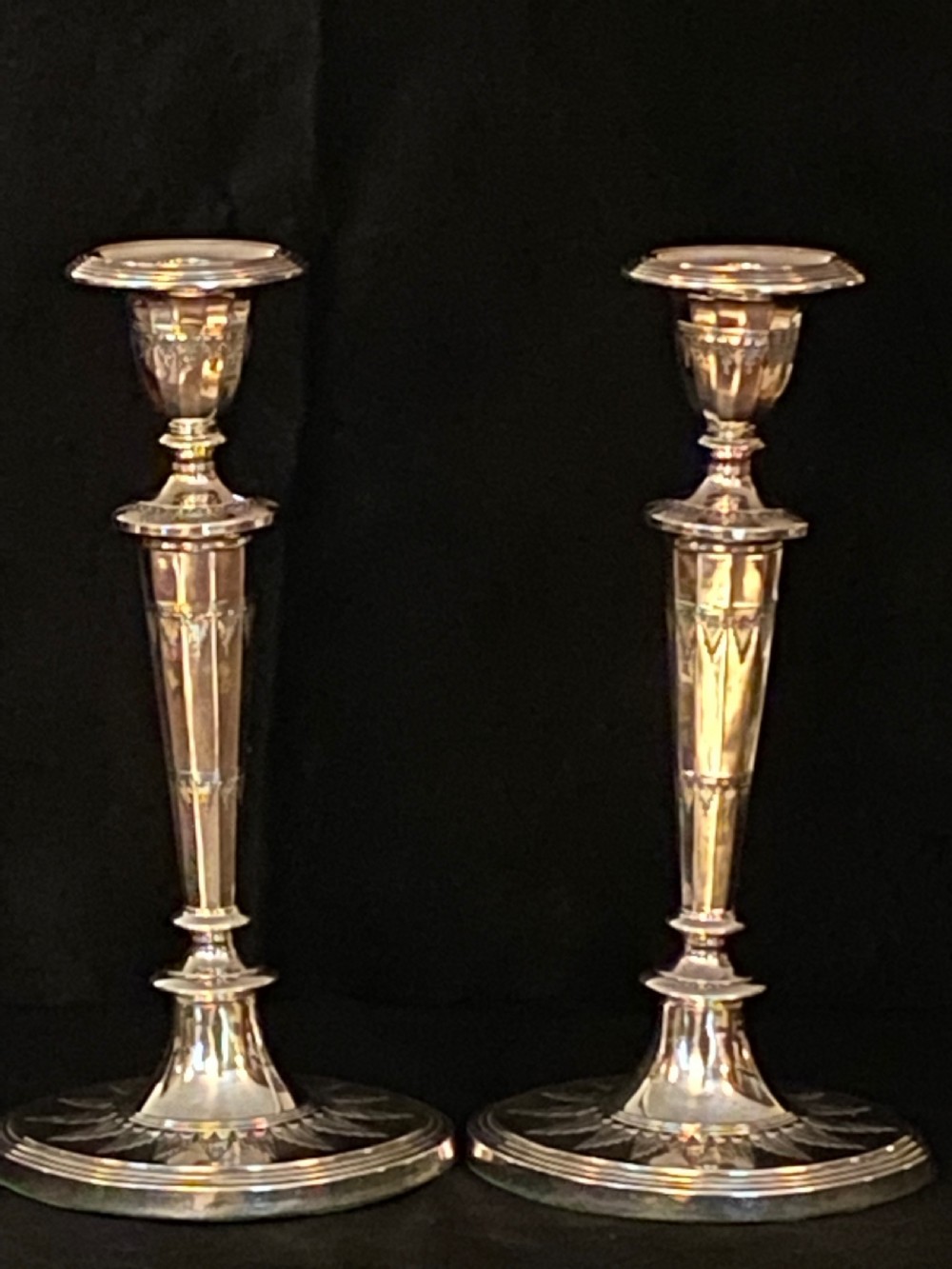 A pair of George III silver-plated candlesticks featuring faceted tapering shafts and circular stepped bases holding white candles. View III