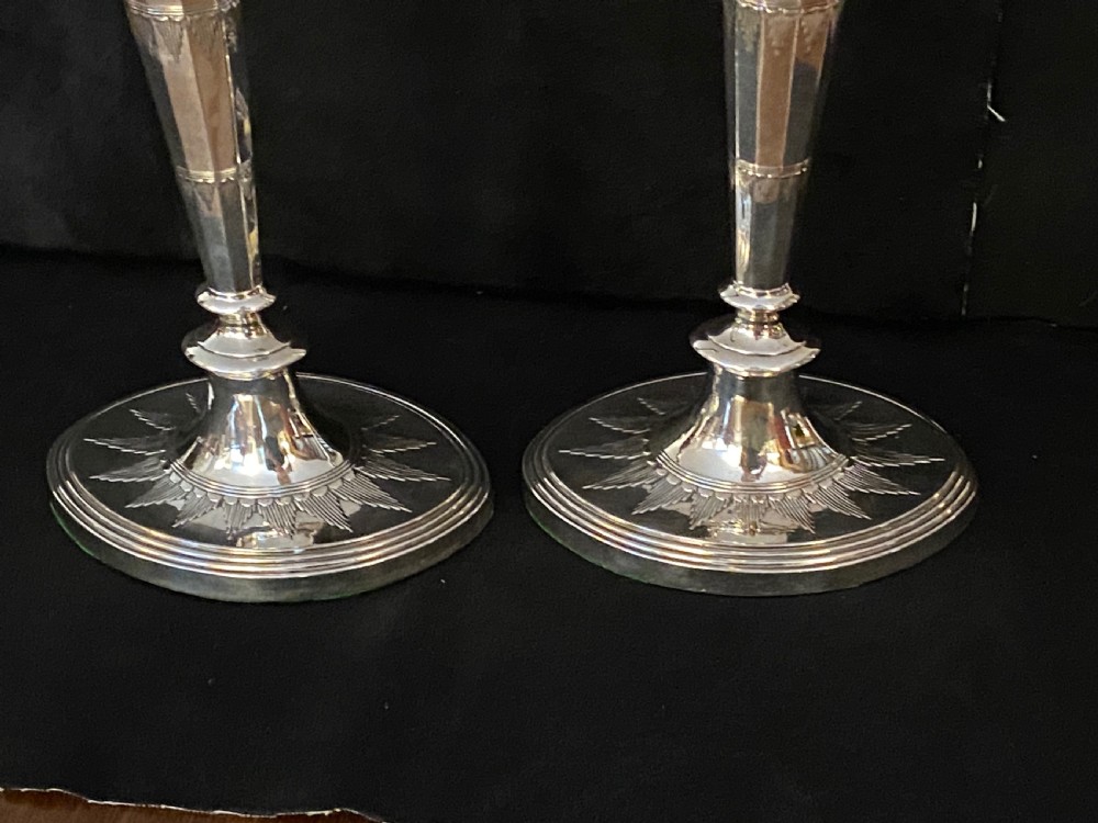 A pair of George III silver-plated candlesticks featuring faceted tapering shafts and circular stepped bases holding white candles. View V