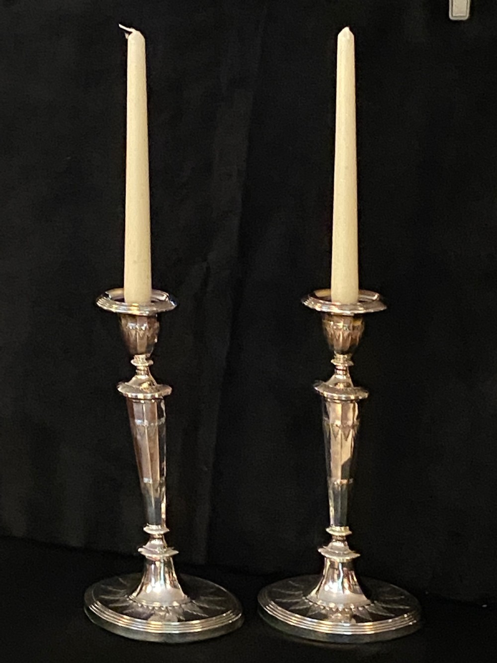 A pair of George III silver-plated candlesticks featuring faceted tapering shafts and circular stepped bases holding white candles.