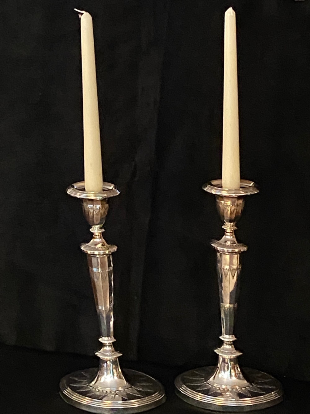 A pair of George III silver-plated candlesticks featuring faceted tapering shafts and circular stepped bases holding white candles. View XIII