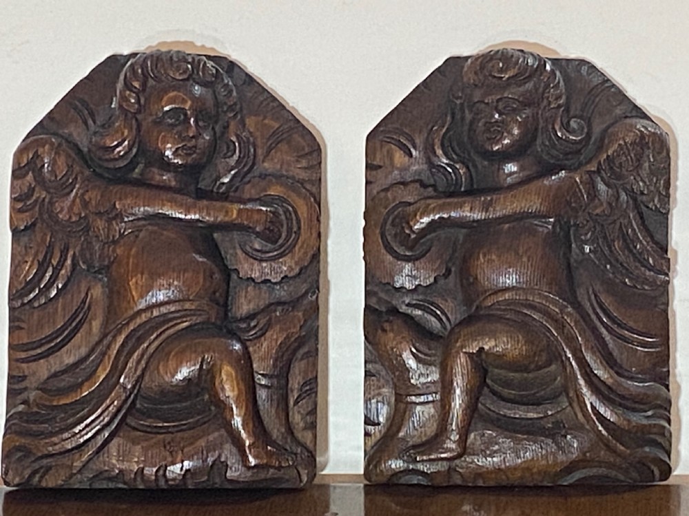 A pair of dark carved oak relief panels depicting winged cherubs playing musical instruments.