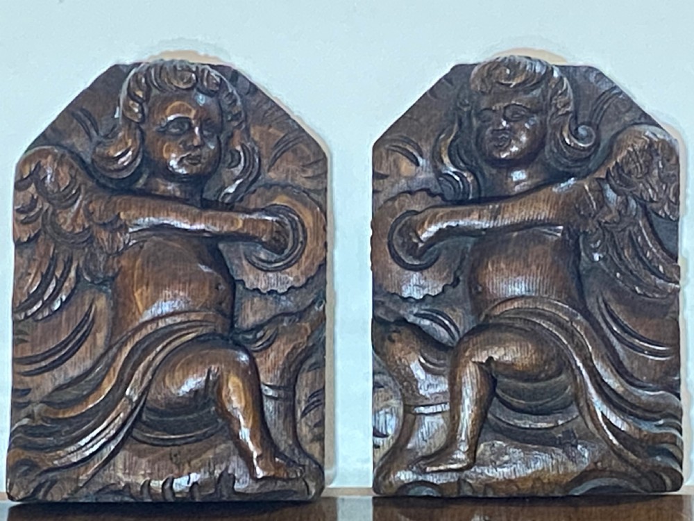 A pair of dark carved oak relief panels depicting winged cherubs playing musical instruments. View II