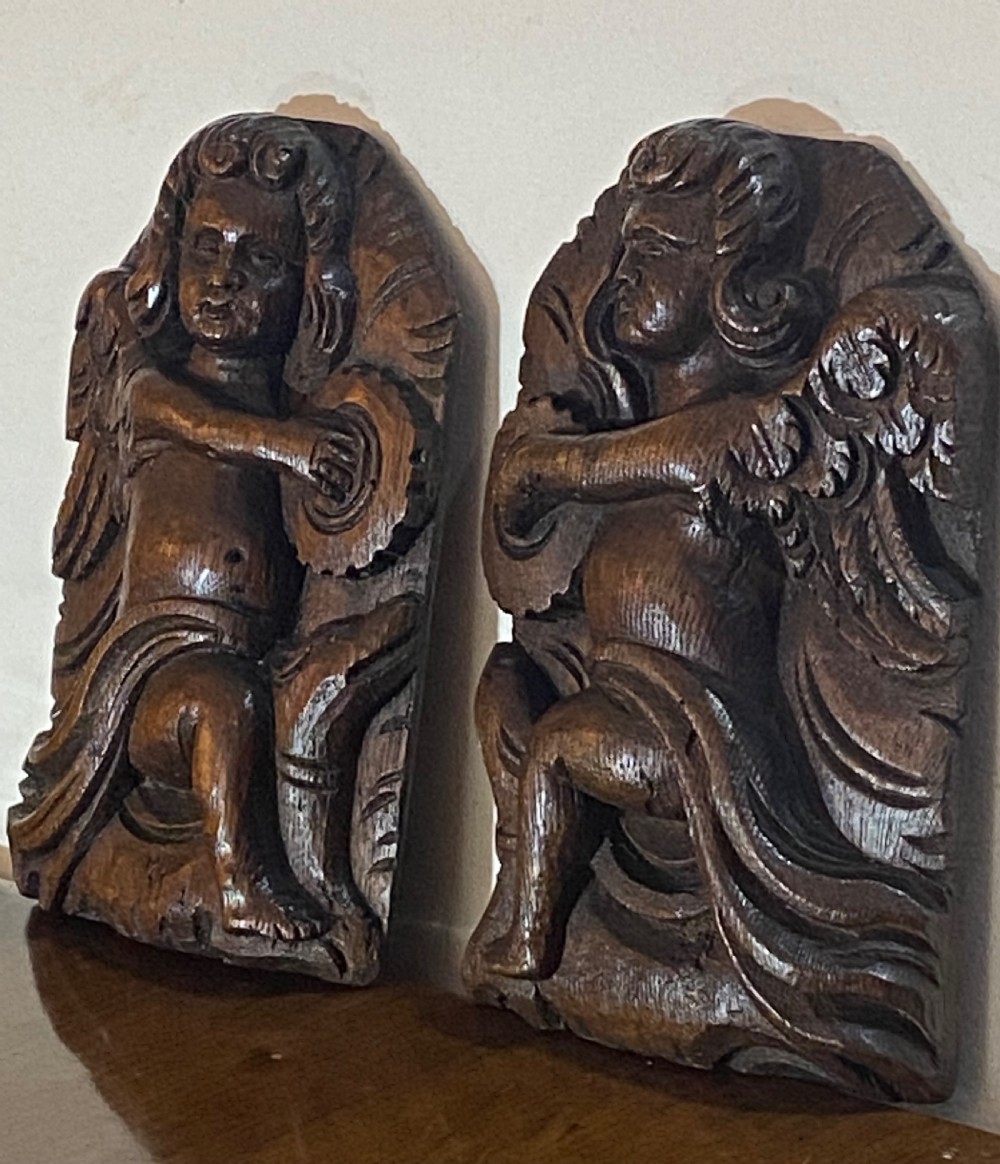 A pair of dark carved oak relief panels depicting winged cherubs playing musical instruments. View III