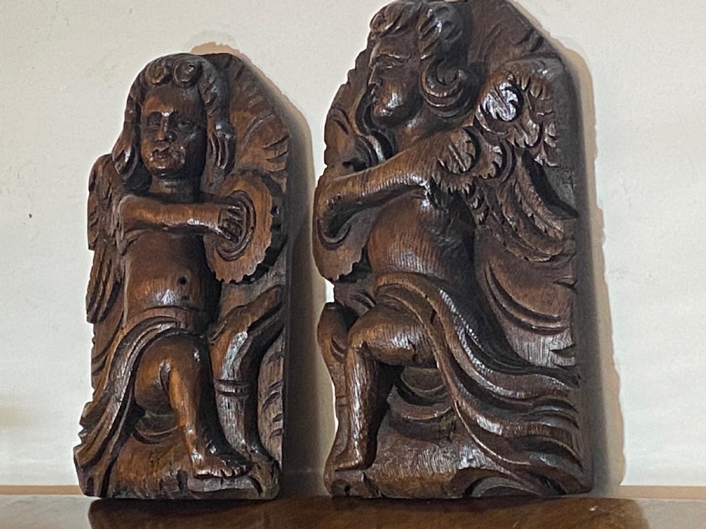 A pair of dark carved oak relief panels depicting winged cherubs playing musical instruments. View IV