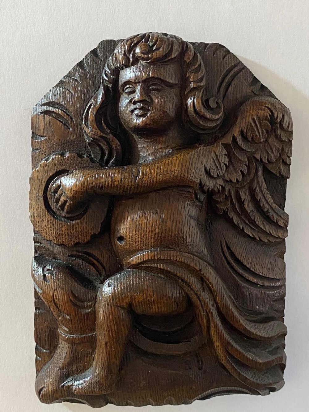 A pair of dark carved oak relief panels depicting winged cherubs playing musical instruments. View V