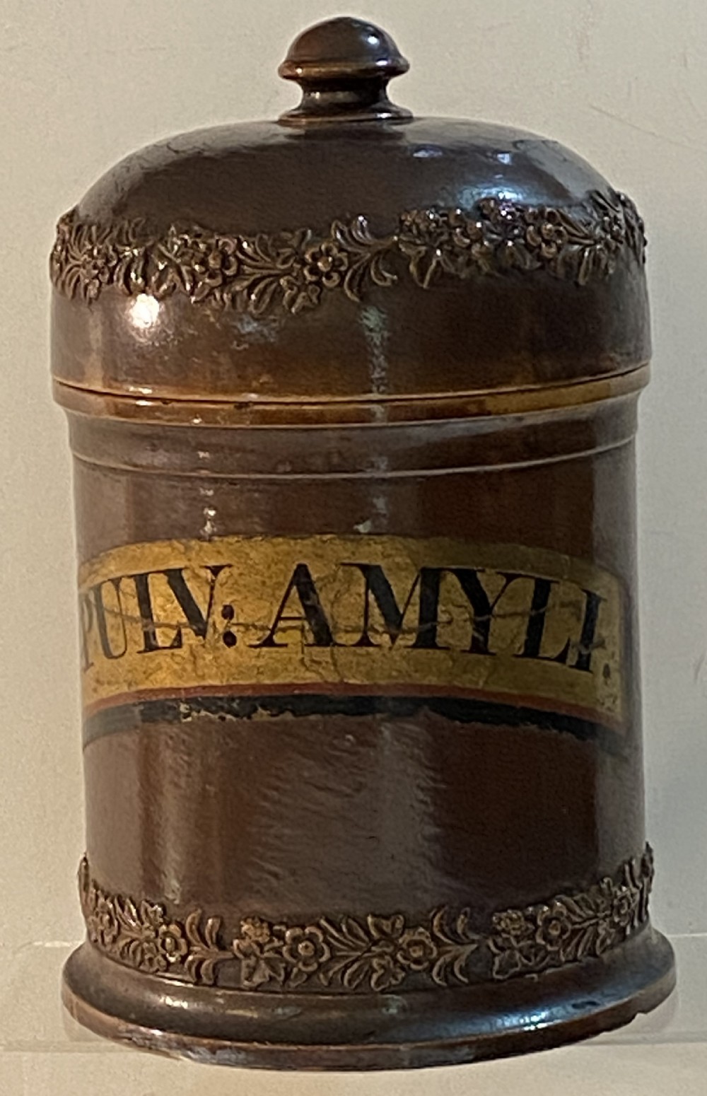 A mid-19th century brown glazed stoneware apothecary jar featuring floral relief borders and a label reading PULV AMYLI.