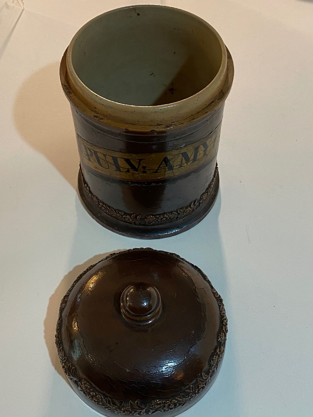 A mid-19th century brown glazed stoneware apothecary jar featuring floral relief borders and a label reading PULV AMYLI. View VII