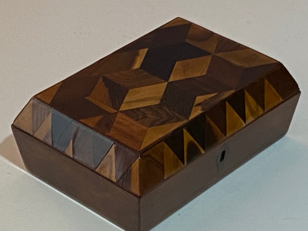 A rectangular wooden box featuring geometric parquetry inlay in contrasting shades of brown wood with a keyhole on the front.