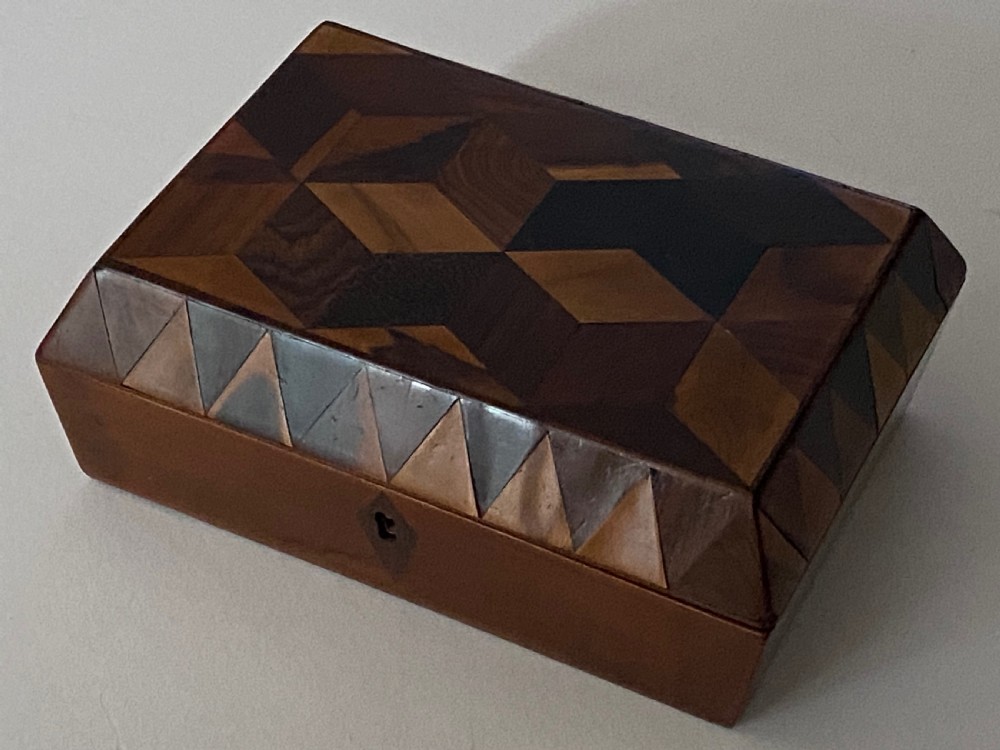 A rectangular wooden box featuring geometric parquetry inlay in contrasting shades of brown wood with a keyhole on the front. View III
