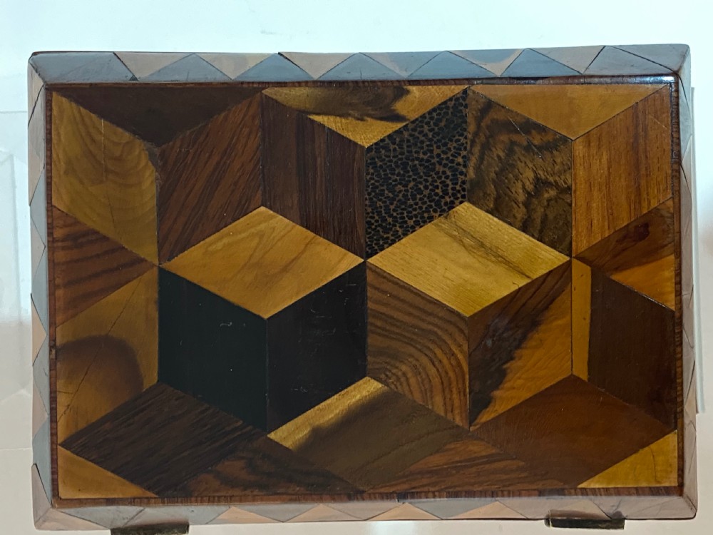 A rectangular wooden box featuring geometric parquetry inlay in contrasting shades of brown wood with a keyhole on the front. View IV