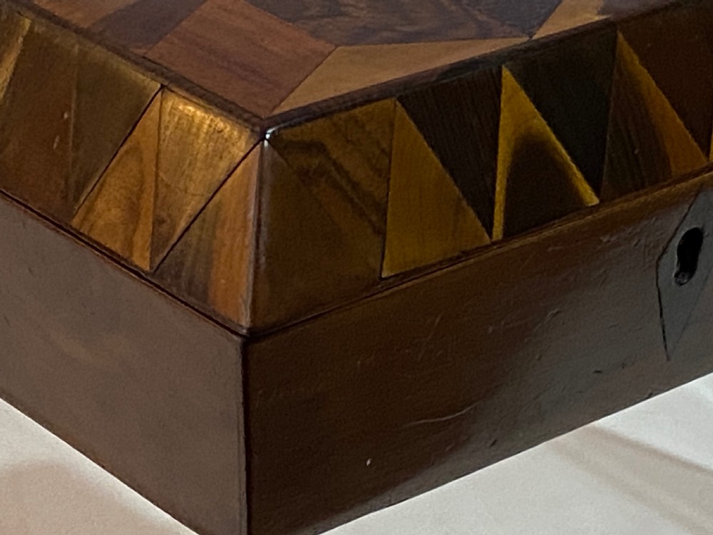 A rectangular wooden box featuring geometric parquetry inlay in contrasting shades of brown wood with a keyhole on the front. View V