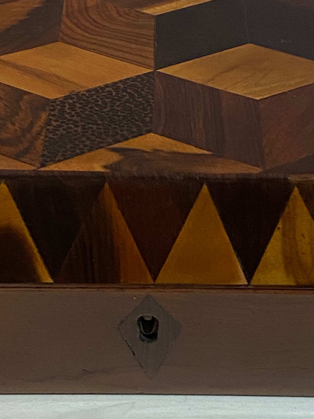A rectangular wooden box featuring geometric parquetry inlay in contrasting shades of brown wood with a keyhole on the front. View VI