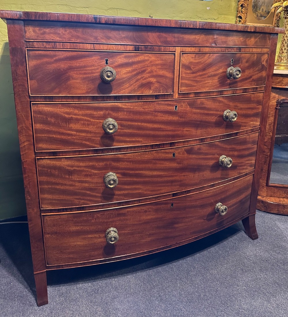A large Regency mahogany bowfront chest featuring two short over three long graduated drawers with decorative brass turned handles on splayed feet.