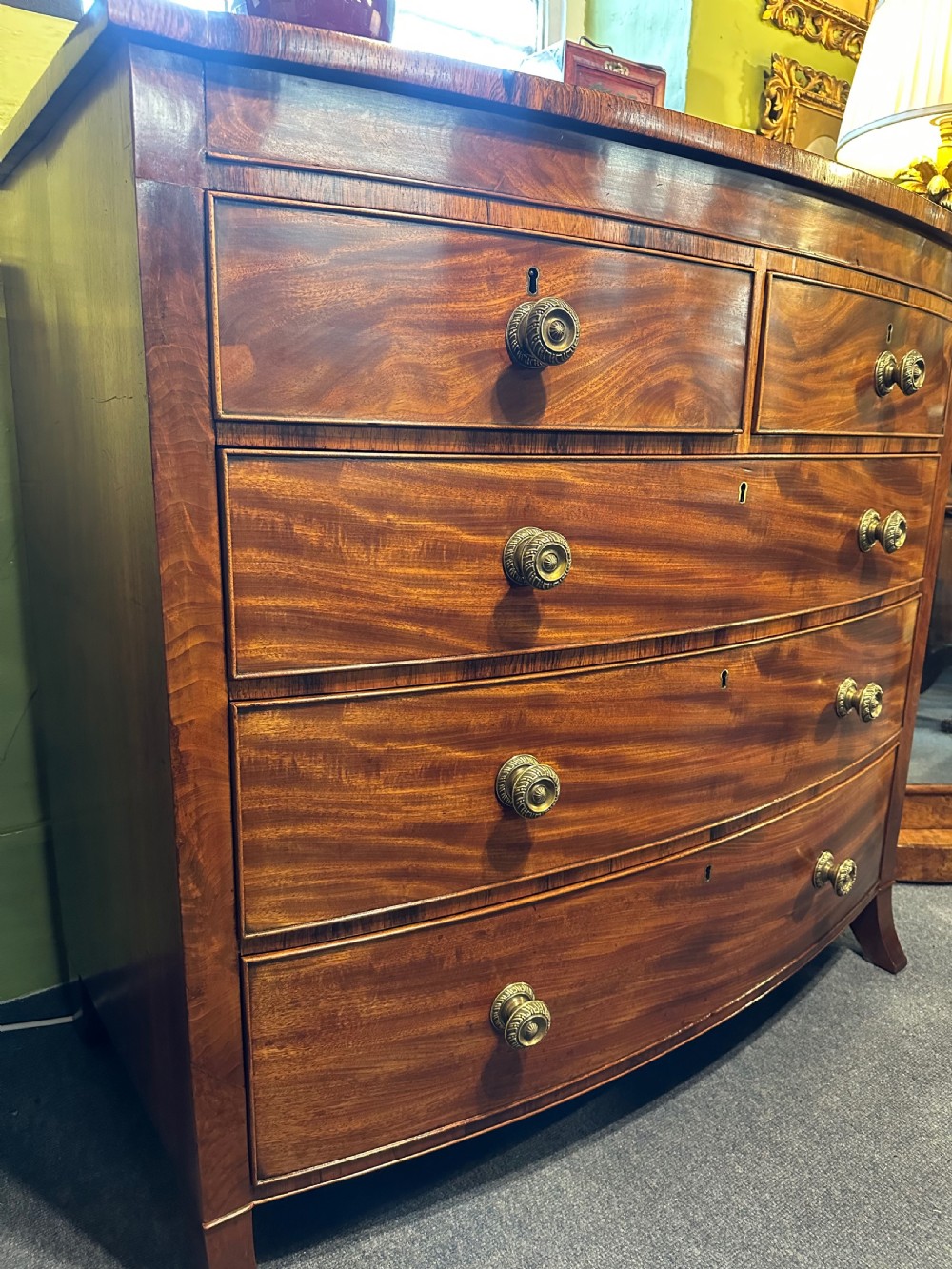 A large Regency mahogany bowfront chest featuring two short over three long graduated drawers with decorative brass turned handles on splayed feet. View V
