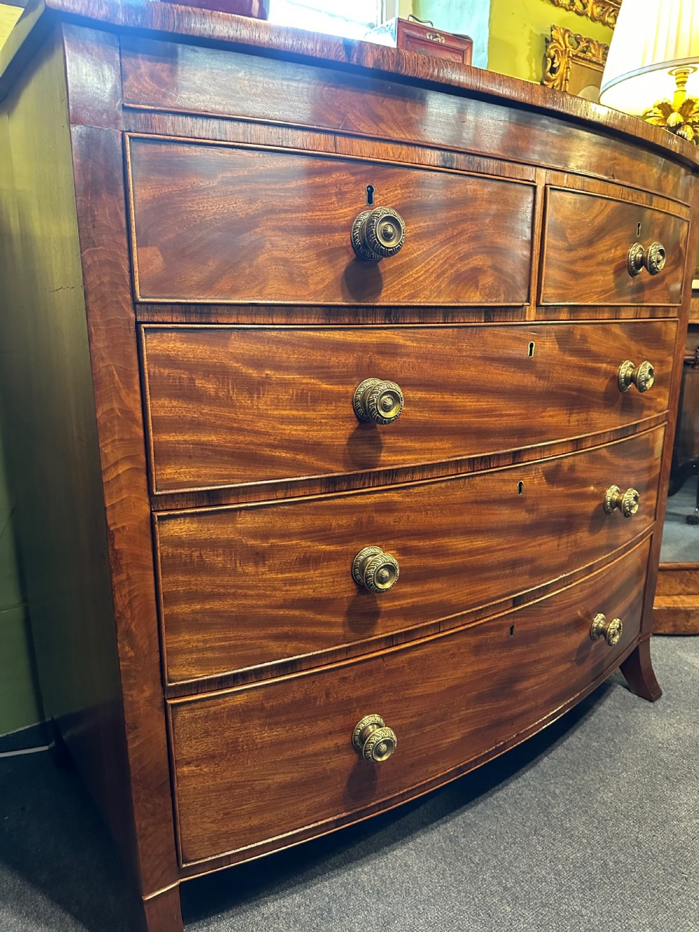 A large Regency mahogany bowfront chest featuring two short over three long graduated drawers with decorative brass turned handles on splayed feet. View VI