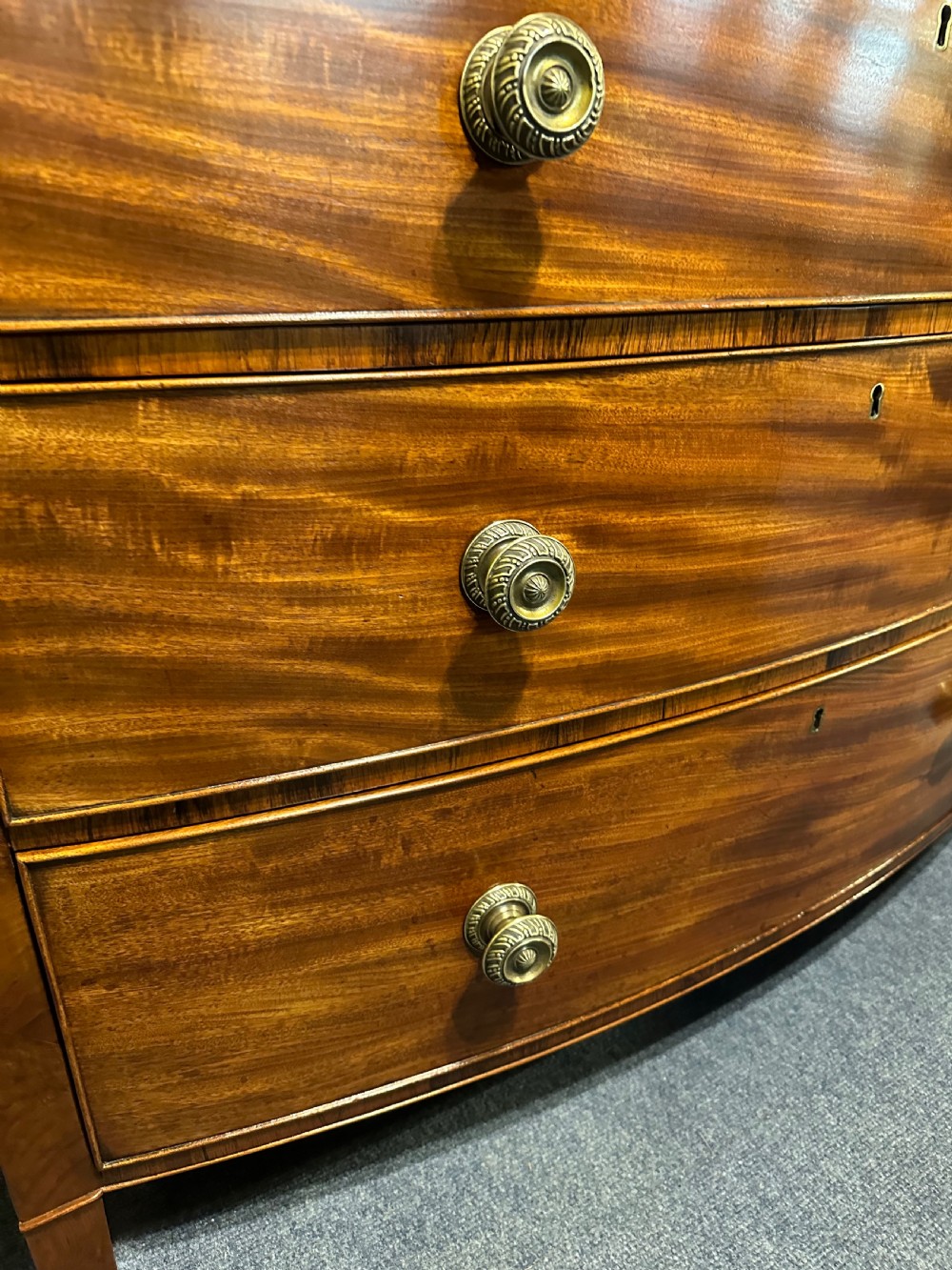 A large Regency mahogany bowfront chest featuring two short over three long graduated drawers with decorative brass turned handles on splayed feet. View VII