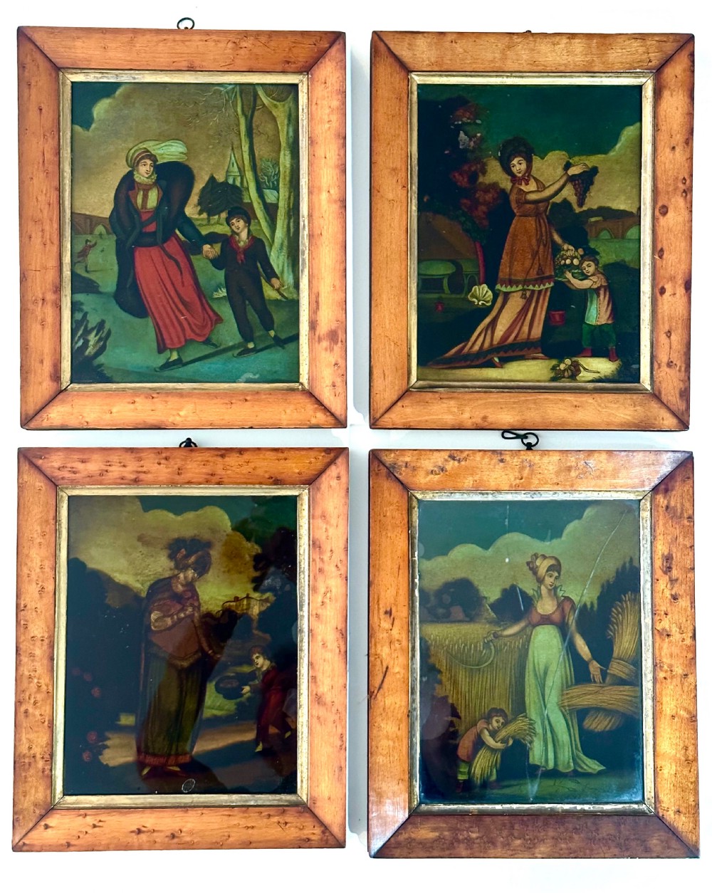 Set of four Regency reverse glass prints depicting figures representing the seasons, framed in birds-eye maple frames with gilt slips.