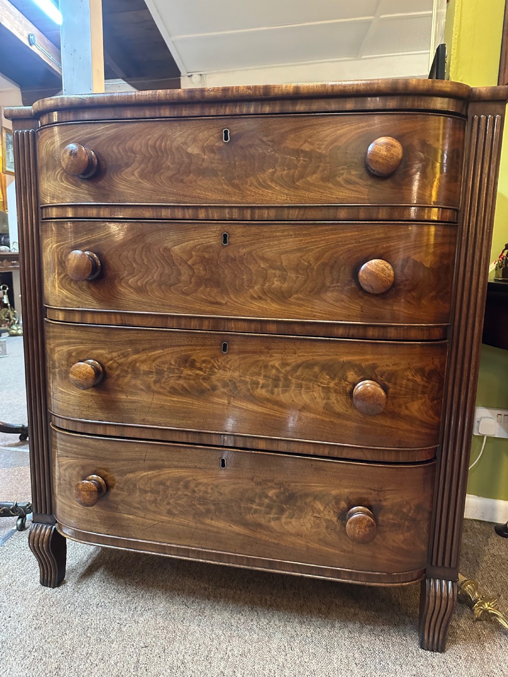 A Regency flame mahogany chest of drawers featuring four graduated bow-front drawers, turned wood handles, and reeded side columns.