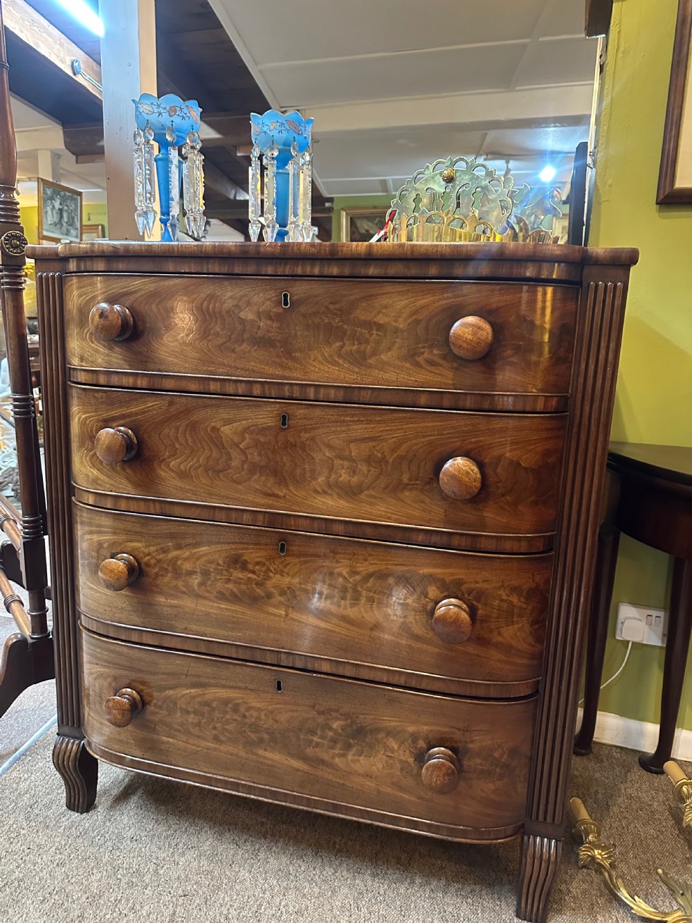 A Regency flame mahogany chest of drawers featuring four graduated bow-front drawers, turned wood handles, and reeded side columns. View II