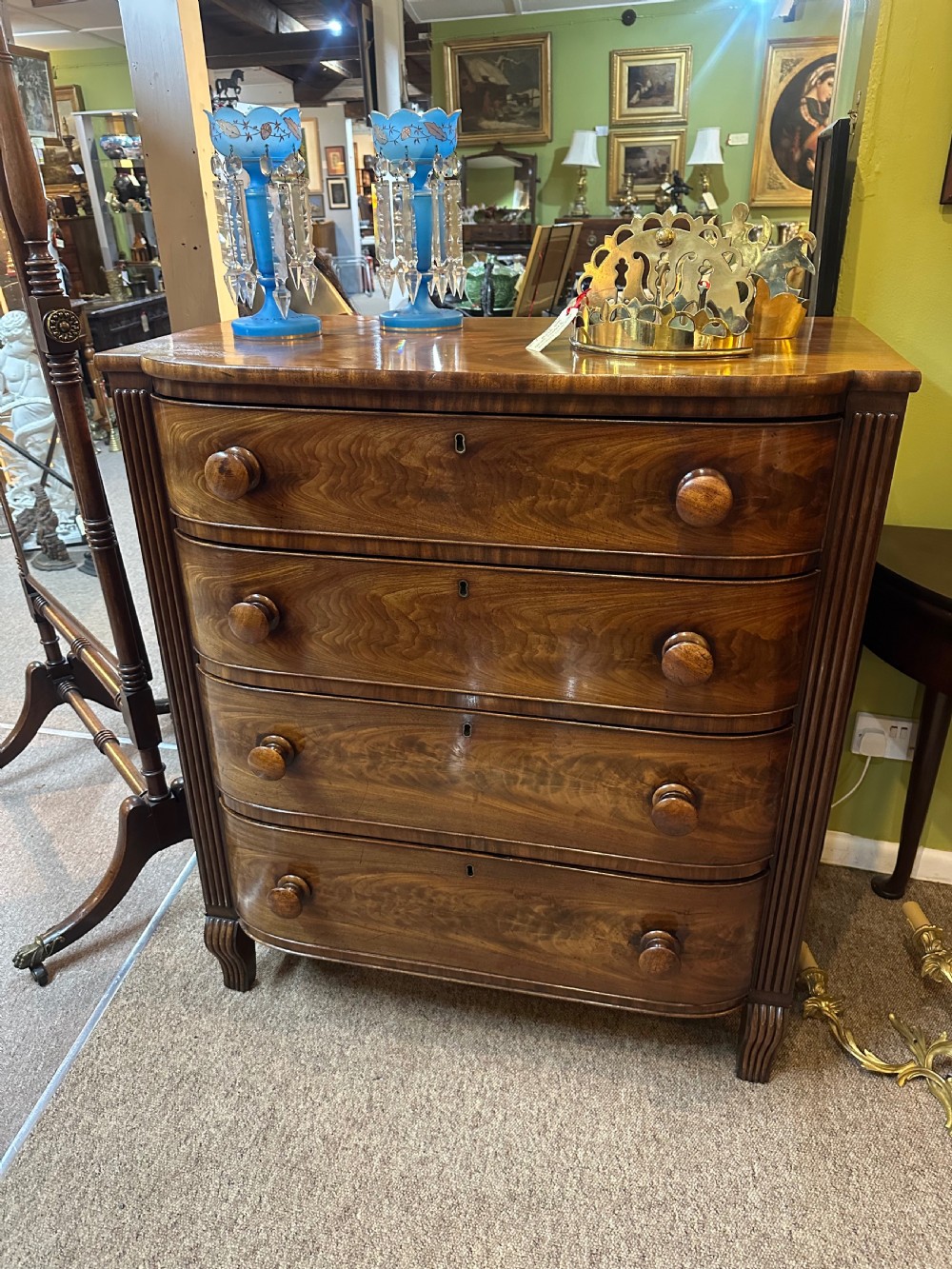 A Regency flame mahogany chest of drawers featuring four graduated bow-front drawers, turned wood handles, and reeded side columns. View III