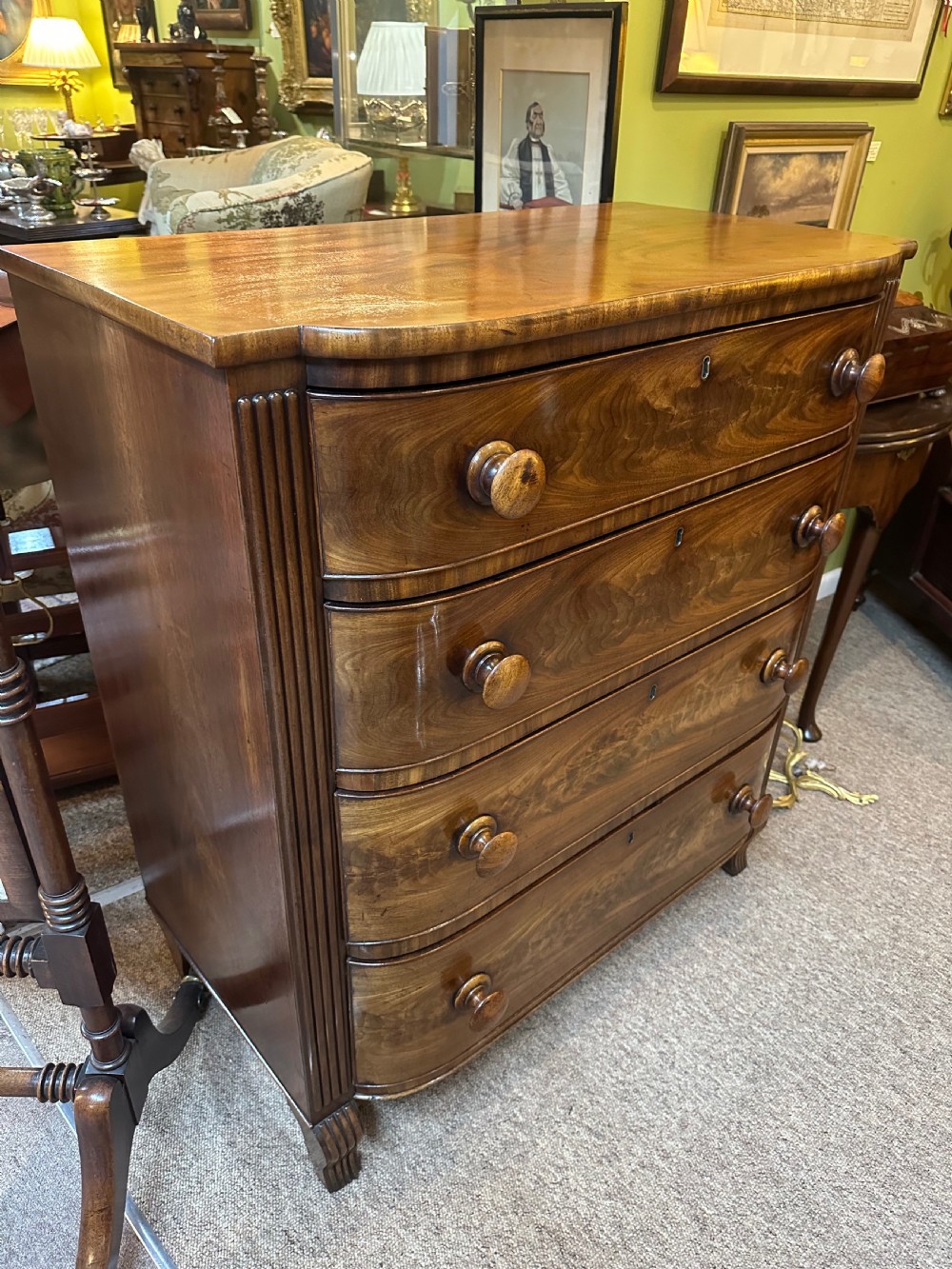 A Regency flame mahogany chest of drawers featuring four graduated bow-front drawers, turned wood handles, and reeded side columns. View VII