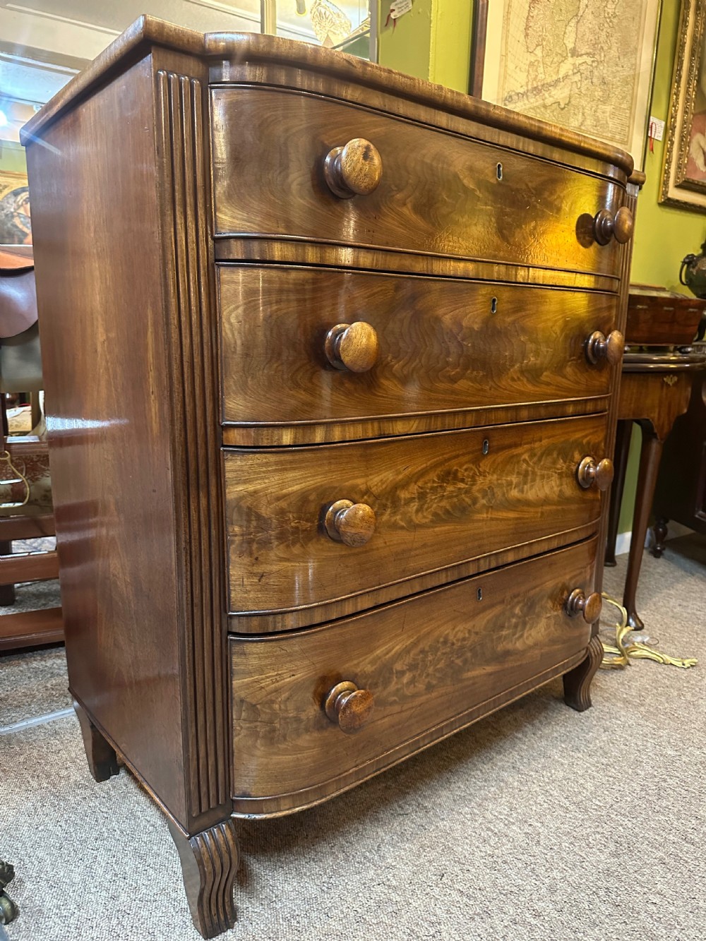 A Regency flame mahogany chest of drawers featuring four graduated bow-front drawers, turned wood handles, and reeded side columns. View VIII