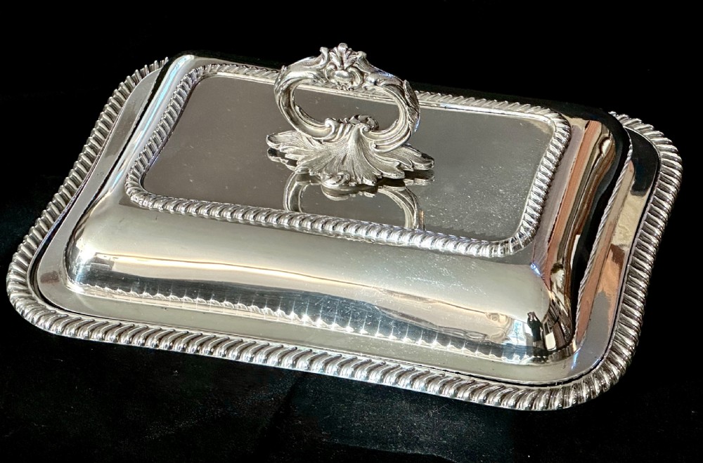 A rectangular silver-plated covered serving dish featuring gadrooned rope borders and a decorative foliage-detailed handle on top.