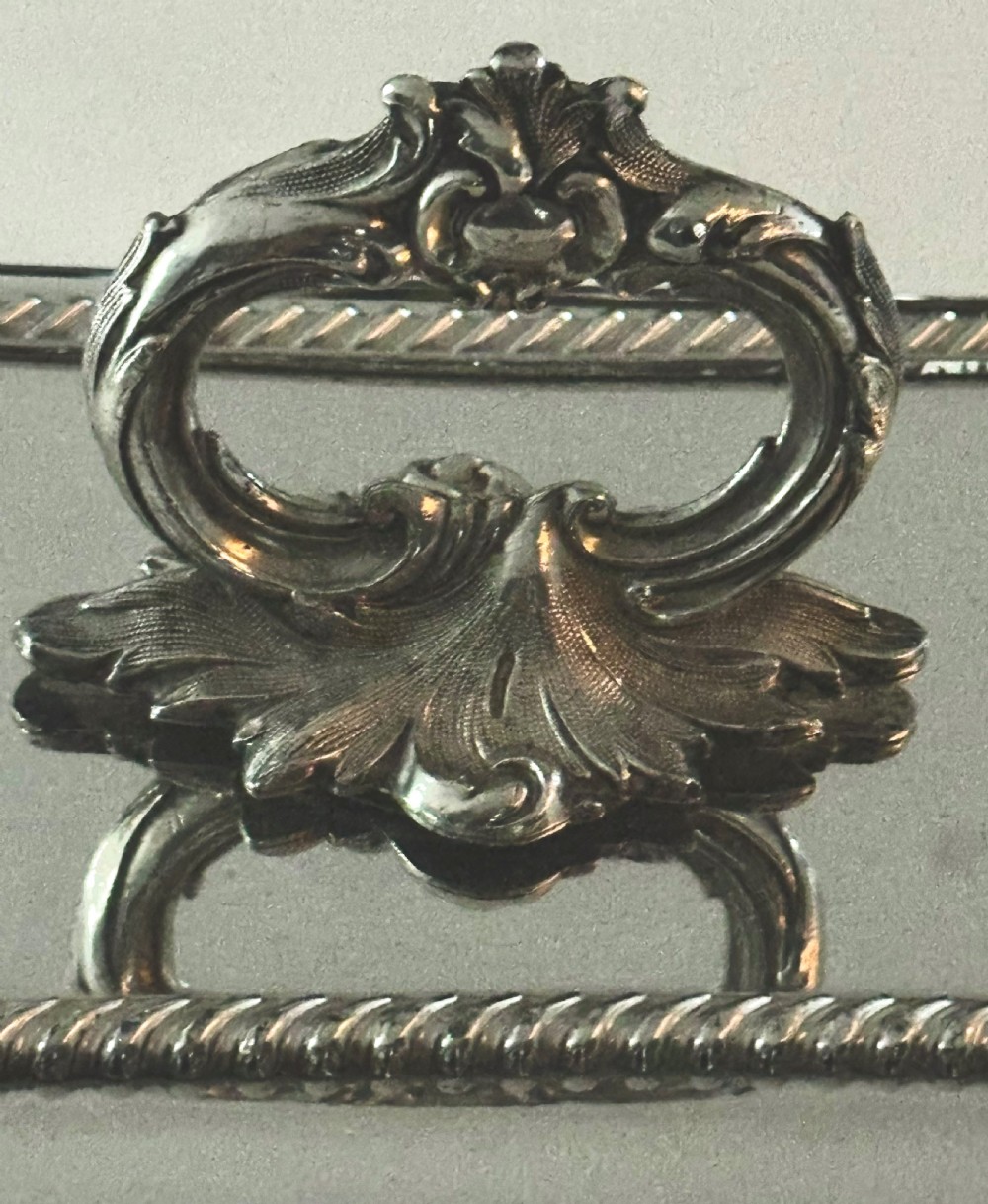 A rectangular silver-plated covered serving dish featuring gadrooned rope borders and a decorative foliage-detailed handle on top. View V