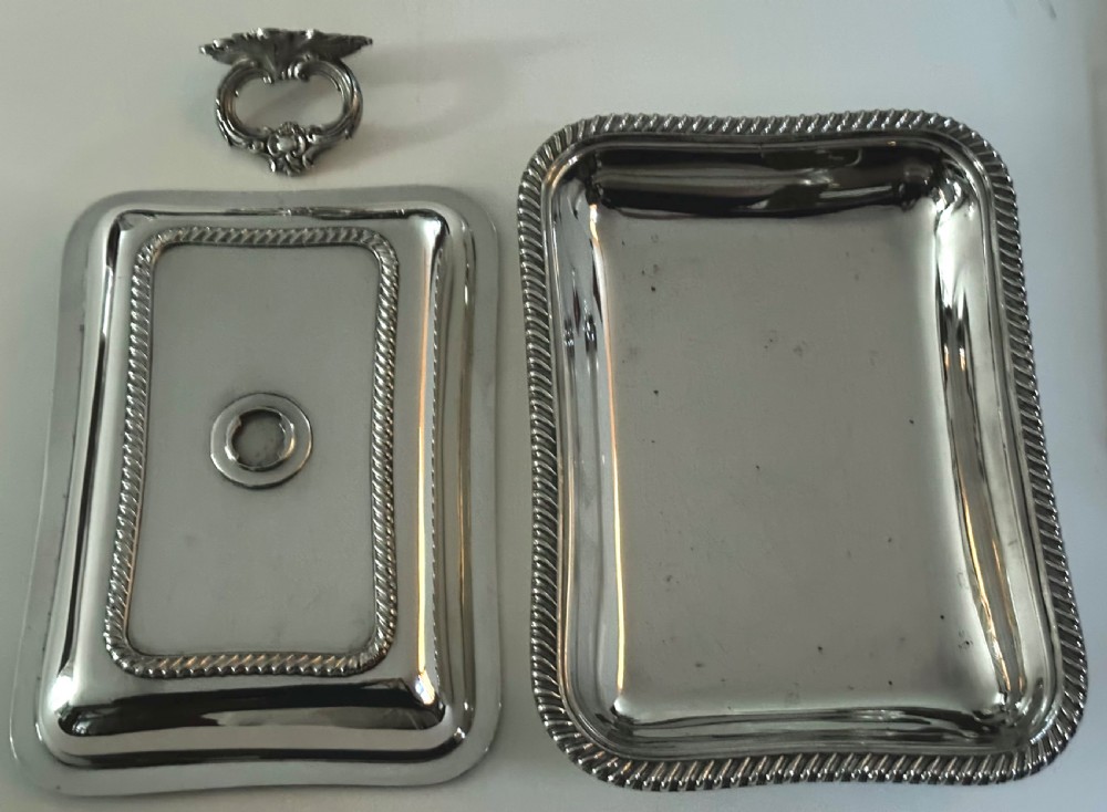 A rectangular silver-plated covered serving dish featuring gadrooned rope borders and a decorative foliage-detailed handle on top. View VI