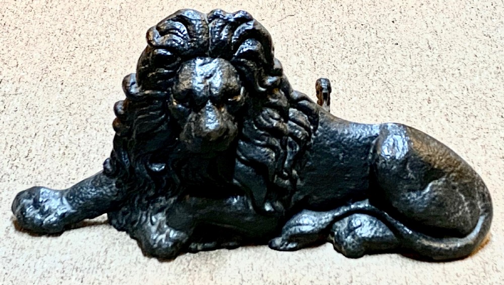 A heavy black cast iron figure depicting a recumbent lion, designed as a boot scraper or doorstop.