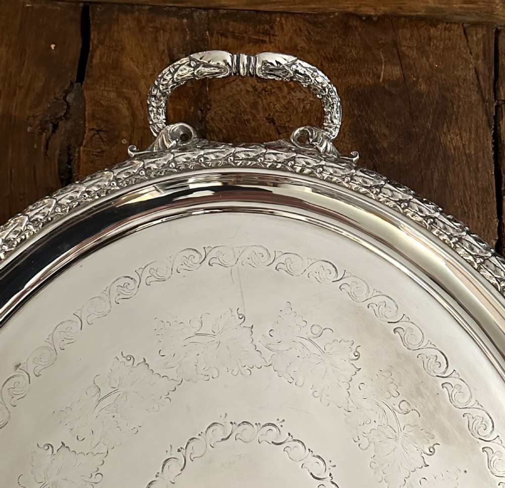 A large oval Edwardian silver-plated serving tray with detailed scrollwork rims, surface foliage engraving, and two cast side handles. View II
