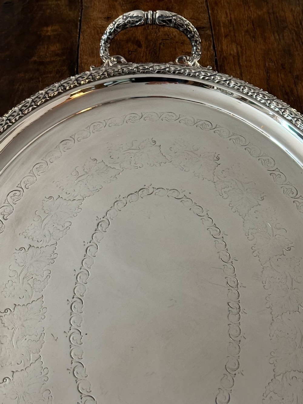 A large oval Edwardian silver-plated serving tray with detailed scrollwork rims, surface foliage engraving, and two cast side handles. View IV