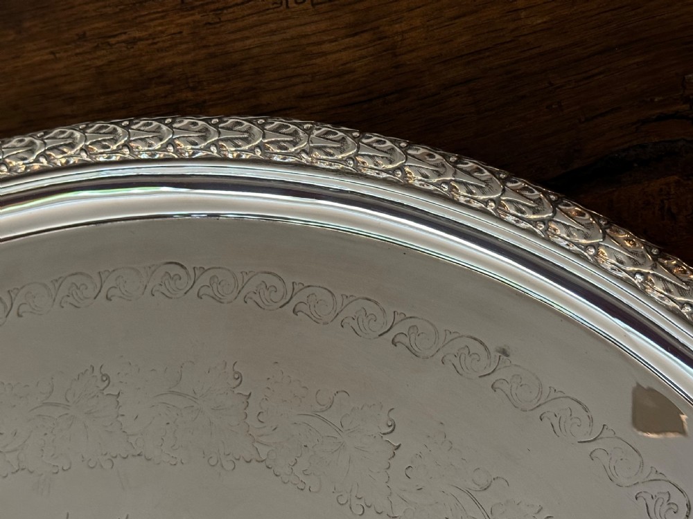 A large oval Edwardian silver-plated serving tray with detailed scrollwork rims, surface foliage engraving, and two cast side handles. View VI